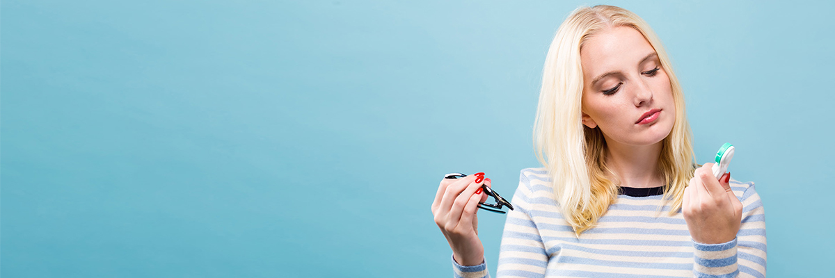 A woman holding a pair of glasses and a contact lens case